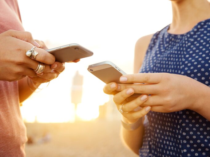 Zwei Frauen tippen an ihrem Smartphone, während die Sonne scheint | © Getty Images/Tim Robberts