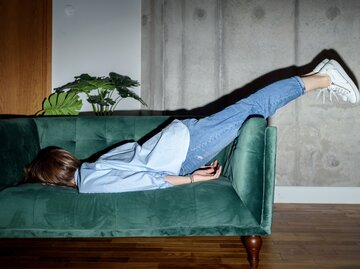 Frau liegt mit dem Gesicht nach unten auf dem Sofa | © GettyImages/	karetoria