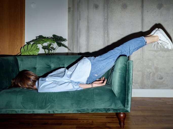 Frau liegt mit dem Gesicht nach unten auf dem Sofa | © GettyImages/	karetoria
