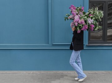 Frau mit Jeanshose trägt einen bunten Blumenstrauß | © GettyImages/Sofia Polukhina