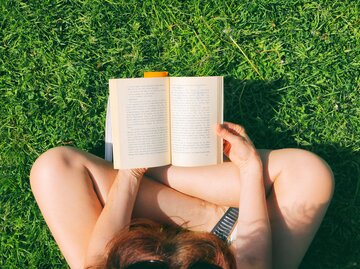 Frau liest in der sommerlichen Wiese ein Buch | © GettyImages/	Katrin Ray Shumakov