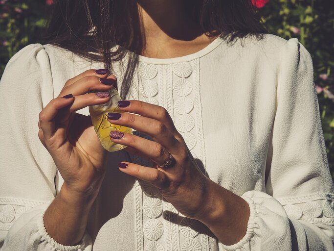 Frau hält in sommerlicher Atmosphäre Parfum in der Hand | © GettyImages/	adrianova_