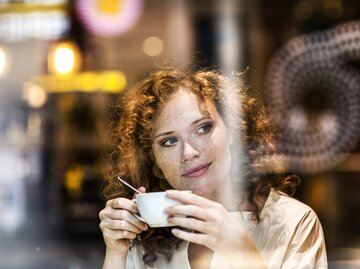 Frau trinkt Kaffee und blickt durch eine Fensterscheibe | © GettyImages/Westend61