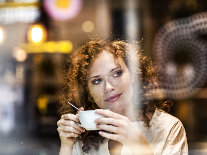 Frau trinkt Kaffee und blickt durch eine Fensterscheibe | © GettyImages/Westend61