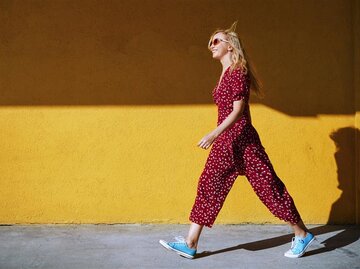 Frau im Jumpsuit läuft vor gelber Wand | © Getty Images/Arman Zhenikeyev