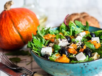 Kürbissalat mit Feta und Oliven und Kürbis im Hintergrund | © AdobeStock/rome2015