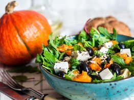 Kürbissalat mit Feta und Oliven und Kürbis im Hintergrund | © AdobeStock/rome2015