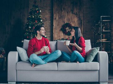 Paar sitzt auf der Couch im weihnachtlichen Wohnzimmer und trinkt Kaffee | © GettyImages/Deagreez