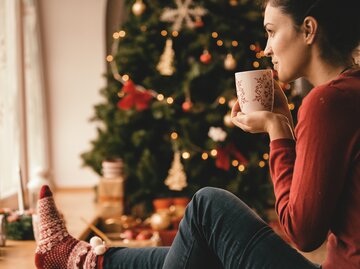 Junge Frau sitzt gemütlich unter dem Tannenbaum | © Getty Images/	fotostorm