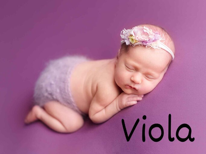 Ein Baby mit Blumenhaarband liegt schlafend auf einer Lila-Decke - unten Rechts im Bild der Mädchenname Viola. | © Adobe Stock/Svetlana