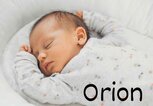 Ein schlafendes Baby liegt entspannt in einem grauen, mit Blumen gemusterten Strampler auf einer weißen Unterlage - rechts unten steht der Jungenname Orion. | © Adobe Stock/Strelciuc