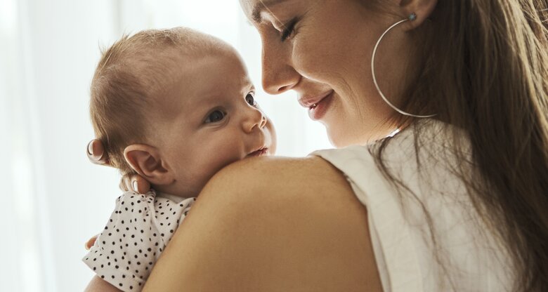 Brünette Frau hält ihr Baby in den Händen, Sprüche zur Geburt | © GettyImages/Nastasic