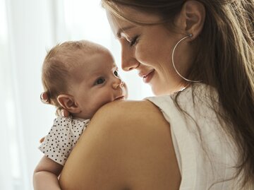 Brünette Frau hält ihr Baby in den Händen, Sprüche zur Geburt | © GettyImages/Nastasic