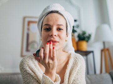 Frau mit Handtuch auf dem Kopf trägt Lippenpflegestift auf | © GettyImages/Hirurg