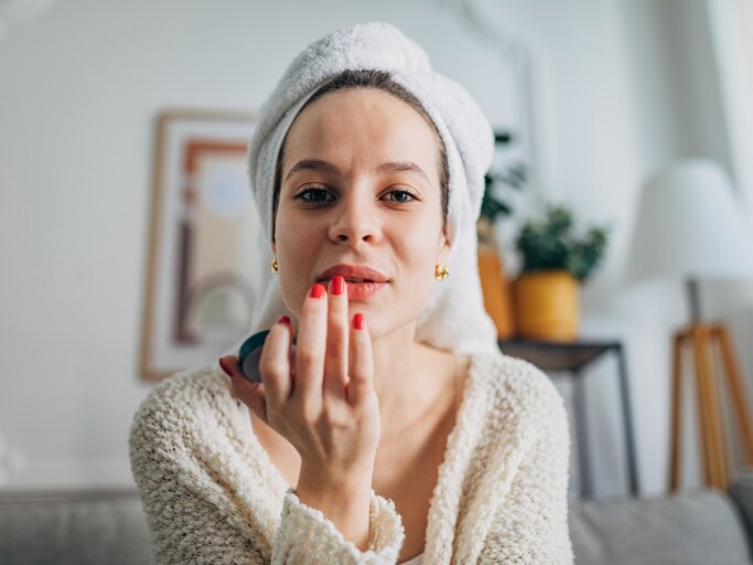 Frau mit Handtuch auf dem Kopf trägt Lippenpflegestift auf | © GettyImages/Hirurg