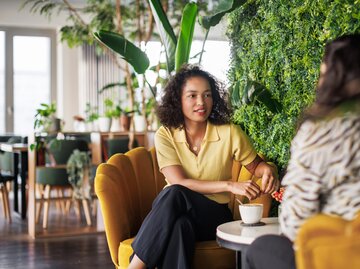 Junge Frau unterhält sich im Café mit einer Freundin | © GettyImages/Tom Werner